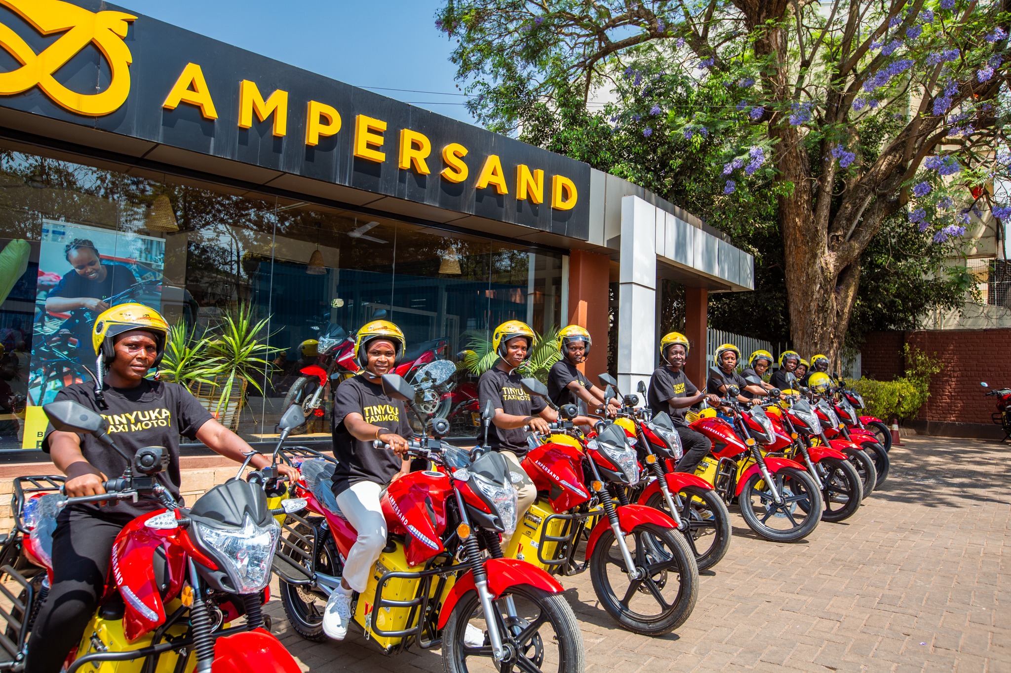 Riders and electric motorcycles outside an Ampersand building.